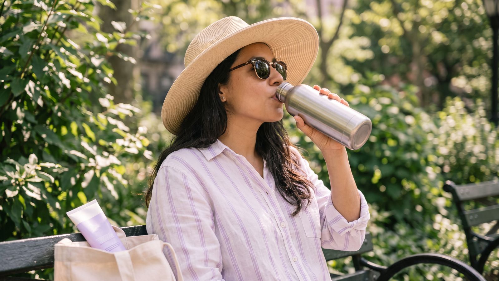 Mujer con sombrero tomando agua en un parque en un día de calor